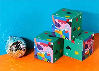 Three custom folding boxes with vibrant branded artwork in a playful studio setting