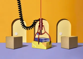 Claw machine grabbing a colorful custom branded shipping box from among plain corrugated boxes